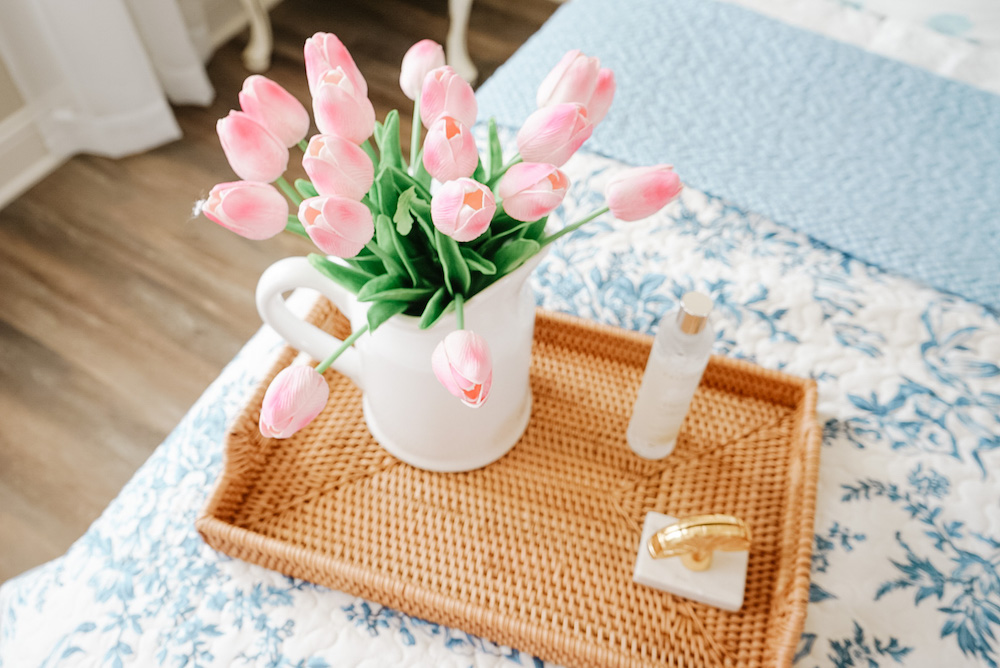 pink faux tulips in a white vase on a tray on top of the bed
